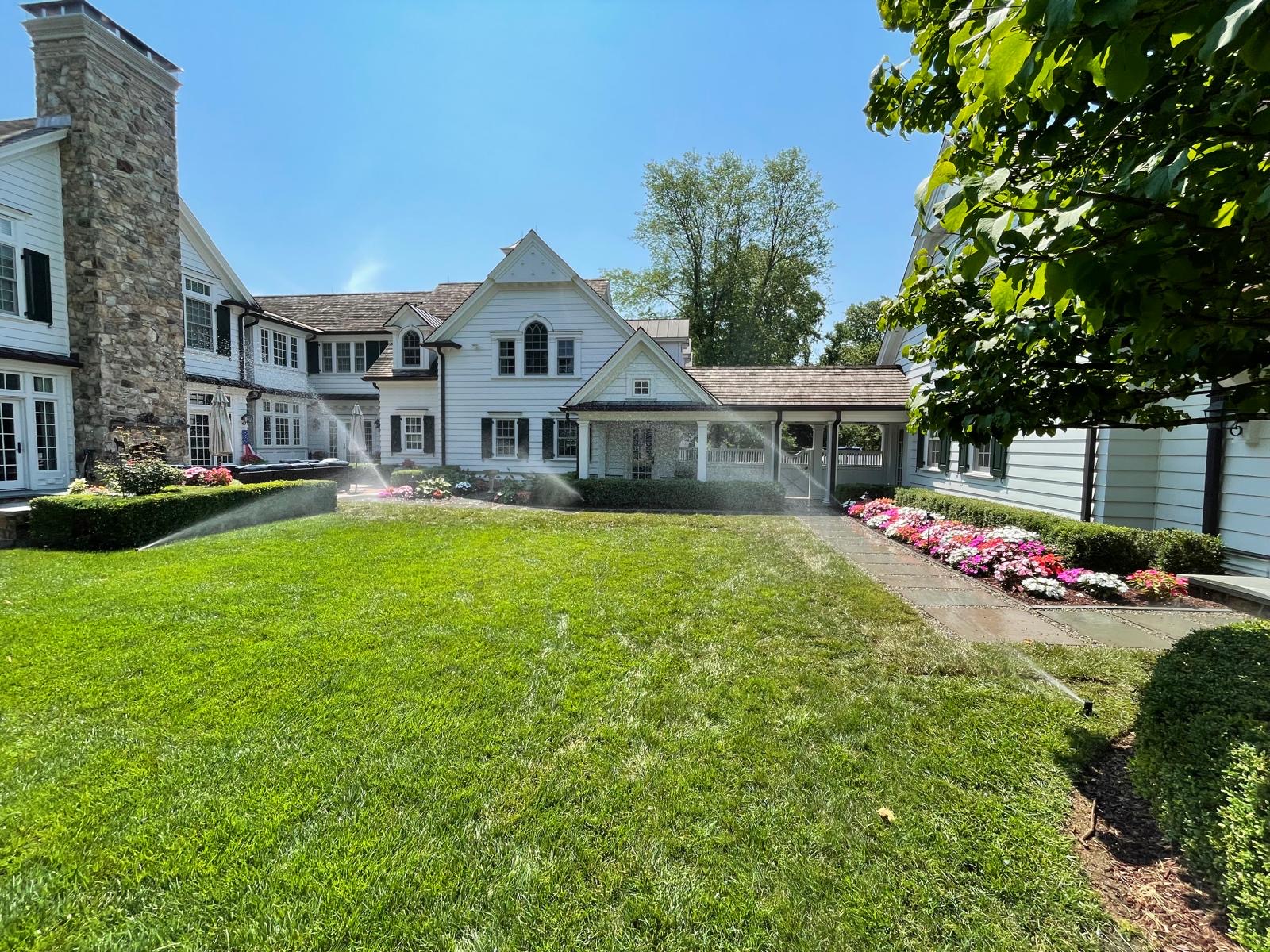 Sprinklers running across a courtyard lawn beside a border of pink and white impatiens
