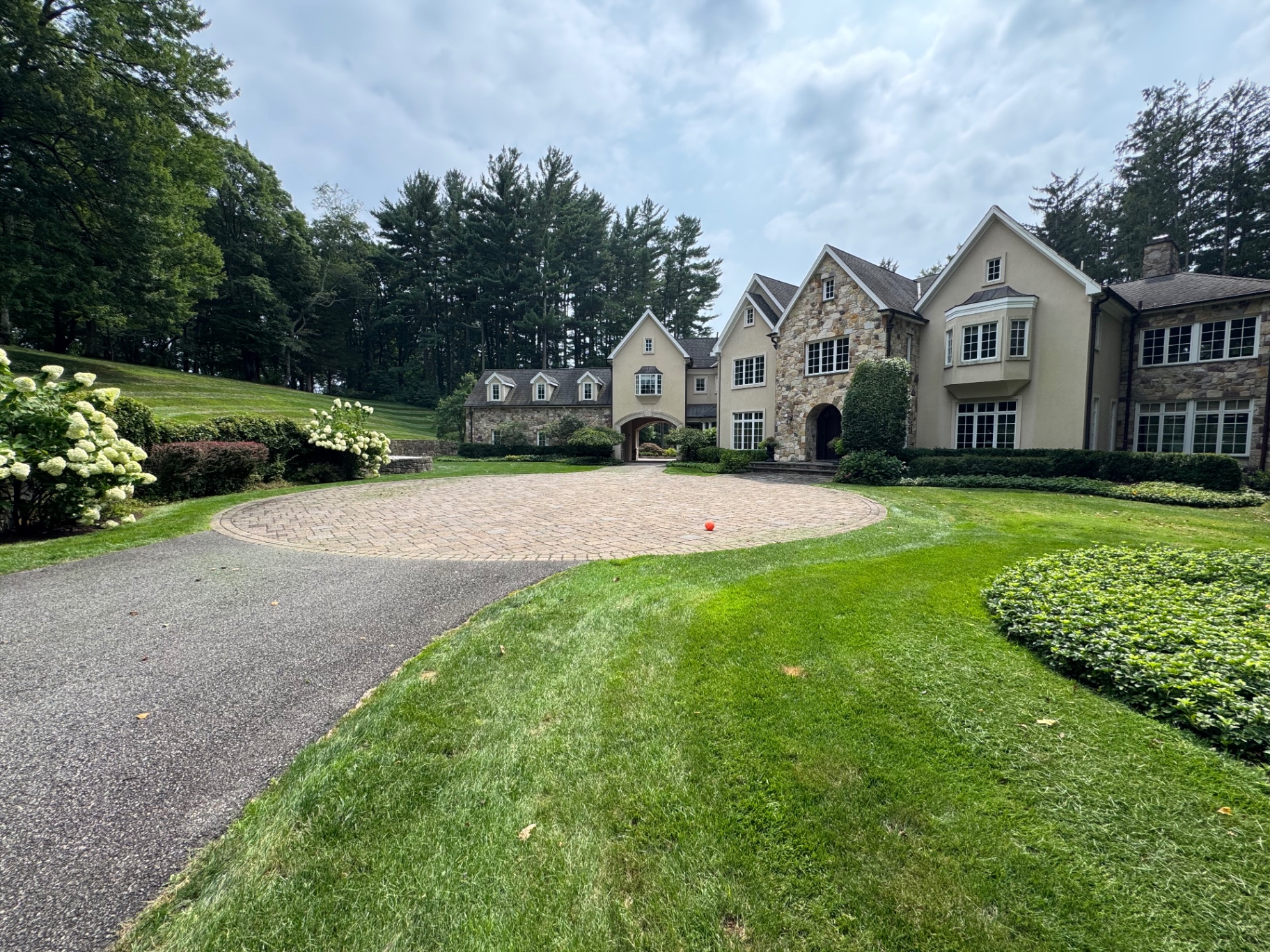 Paver circular driveway framed by hydrangeas, groundcover beds and a sweeping maintained lawn