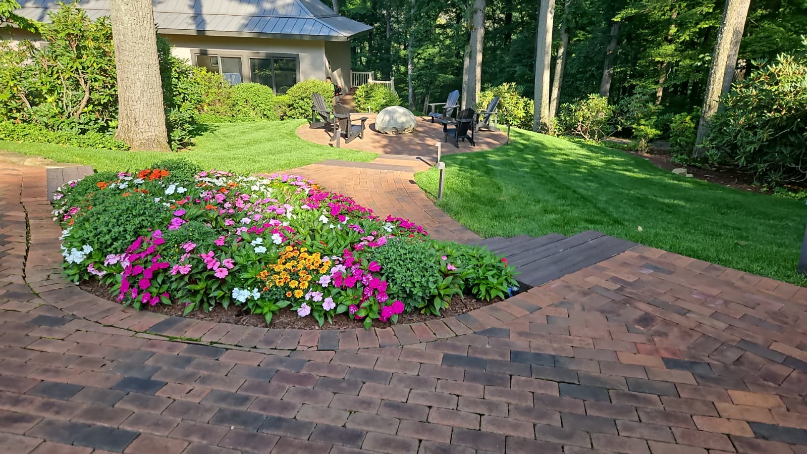 Island planting bed of pink, white and orange annuals within a brick patio near a shaded fire pit terrace
