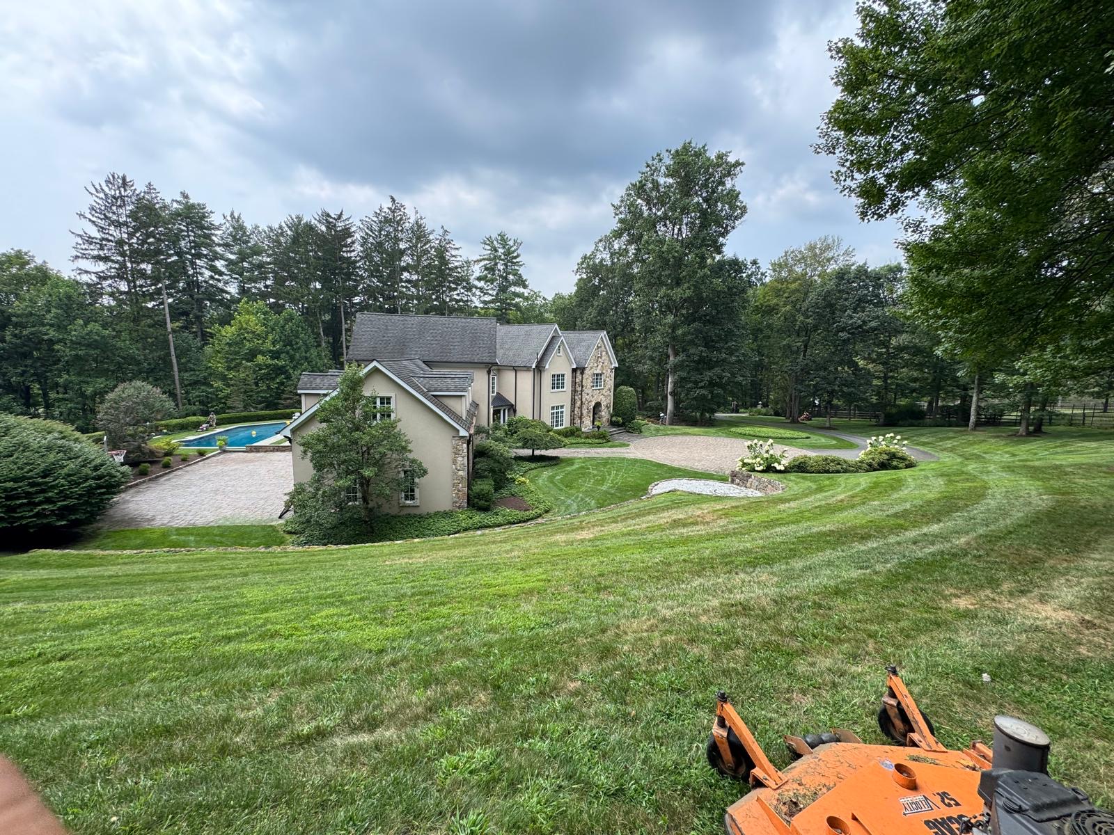 View from a mower over a freshly cut hillside lawn above a paver pool patio