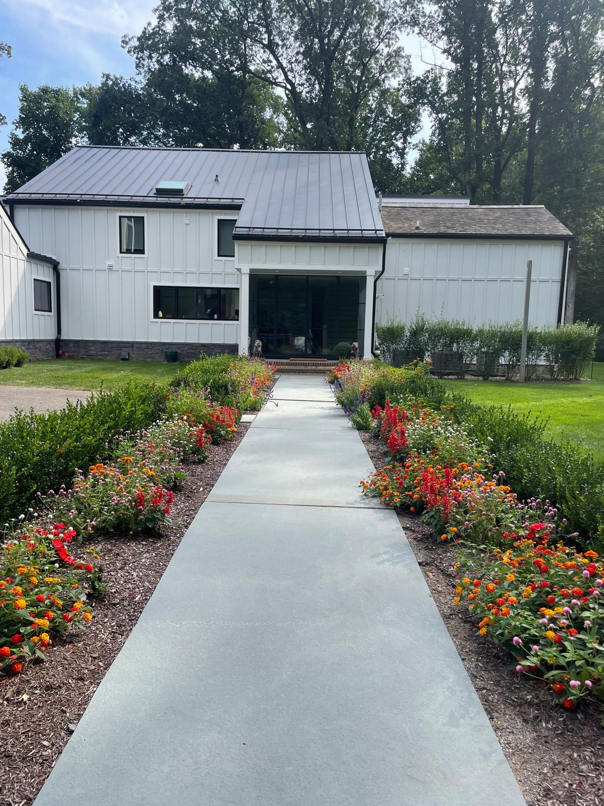 Wide bluestone entry walkway lined with vivid annual flower beds and clipped boxwood